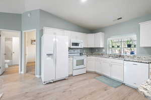 Kitchen with visible vents, vaulted ceiling, a sink, white cabinets, and white appliances