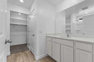 Full bath featuring wood finished floors, vanity, visible vents, a walk in closet, and baseboards