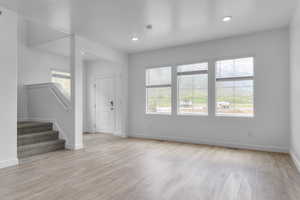 Unfurnished living room featuring stairway, light wood finished floors, baseboards, and visible vents