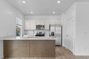 Kitchen featuring a sink, a peninsula, appliances with stainless steel finishes, light countertops, and light wood-style floors