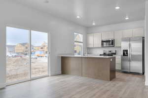 Kitchen with a peninsula, stainless steel appliances, recessed lighting, light countertops, and light wood-style floors