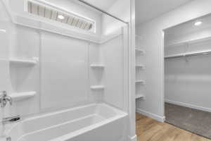 Bathroom featuring baseboards, wood finished floors, shower / washtub combination, and a walk in closet