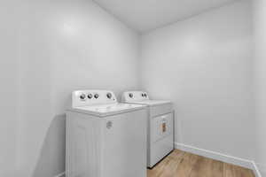 Laundry room with washer and clothes dryer, laundry area, baseboards, and light wood-type flooring