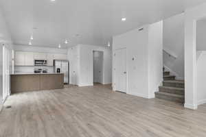Unfurnished living room with recessed lighting, baseboards, light wood finished floors, visible vents, and stairway