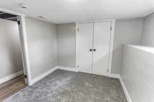 Unfurnished bedroom with a textured ceiling, visible vents, baseboards, a closet, and carpet flooring