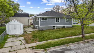View of side of home featuring an outdoor structure, a yard, a shed, and roof with shingles
