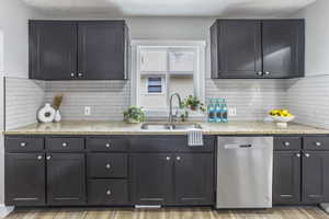 Kitchen with a sink, light stone countertops, backsplash, and dishwasher