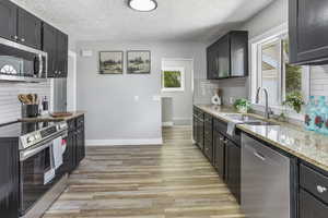 Kitchen featuring a sink, backsplash, light stone countertops, and stainless steel appliances