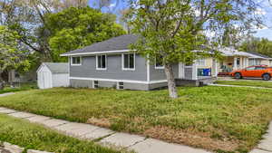 View of front of house with an outdoor structure, fence, a front yard, roof with shingles, and a shed