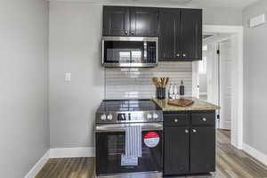 Kitchen with dark cabinetry, baseboards, appliances with stainless steel finishes, and tasteful backsplash