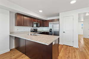 Kitchen with stainless steel appliances, light wood-style floors, a sink, and a peninsula