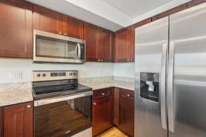 Kitchen featuring appliances with stainless steel finishes, light stone countertops, light wood finished floors, and reddish brown cabinets