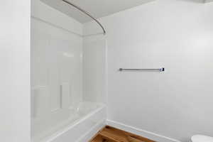 Full bathroom with baseboards, shower / bathing tub combination, toilet, and wood finished floors