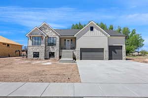 View of front facade with board and batten siding, an attached garage, driveway, and stone siding