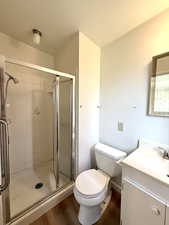 Full bath with vanity, toilet, wood finished floors, and a stall shower