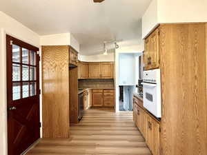 Kitchen featuring brown cabinets, light wood finished floors, dishwasher, decorative backsplash, and white oven