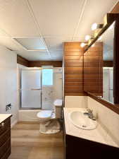 Bathroom featuring vanity, wood finished floors, toilet, shower / bath combination with glass door, and baseboards