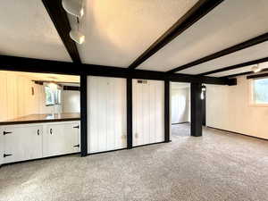 Unfurnished living room with carpet, beam ceiling, a textured ceiling, and visible vents