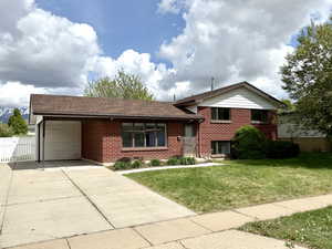 Split level home featuring concrete driveway, brick siding, a gate, and a front lawn