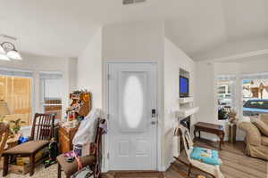Entryway with visible vents, a fireplace, baseboards, light wood finished floors, and vaulted ceiling