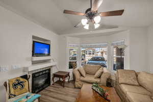 Living area featuring ceiling fan, a fireplace, vaulted ceiling, and wood finished floors