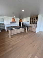 Kitchen featuring dark countertops, a textured ceiling, decorative backsplash, light wood-type flooring, and high quality fridge