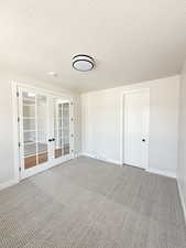 Empty room with french doors, a textured ceiling, visible vents, baseboards, and carpet flooring