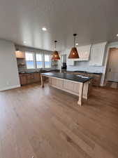Kitchen featuring decorative backsplash, wood finished floors, dark countertops, a center island, and a textured ceiling