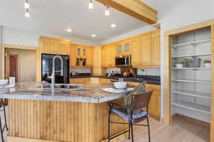 Kitchen featuring stainless steel microwave, a breakfast bar, light wood-type flooring, and black fridge, pantry storage