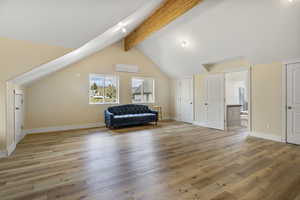 Interior space with vaulted ceiling with beams, baseboards, light wood-style flooring, and a wall mounted AC