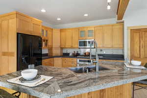 Kitchen with black fridge with ice dispenser, glass insert cabinets, a kitchen bar, stainless steel microwave, and a sink