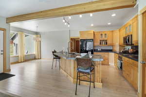 Kitchen with dark countertops, beam ceiling, a sink, a breakfast bar, and stainless steel appliances