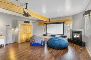 Home theater with beam ceiling, wood-type flooring, a glass covered fireplace, recessed lighting