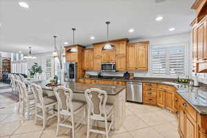 Kitchen with appliances with stainless steel finishes, a center island, a chandelier, dark stone counters, and light tile patterned flooring