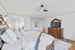 Bedroom featuring crown molding, ceiling fan, arched walkways, baseboards, and wood finished floors