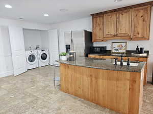 Kitchen with brown cabinetry, washing machine and clothes dryer, black microwave, a sink, and stainless steel fridge