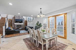 Dining area featuring a notable chandelier, a fireplace, light tile patterned floors, visible vents, and stairway