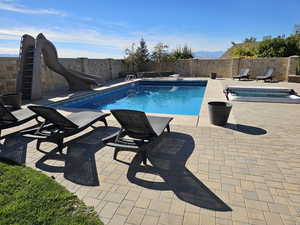 View of swimming pool featuring a water slide, a fenced backyard, a fenced in pool, an in ground hot tub, and a patio area