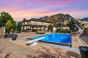 Pool with a diving board, a pergola, a water slide, a mountain view, and a patio