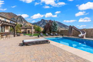 View of pool featuring a patio area, a mountain view, a water slide, and outdoor dry bar