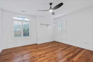Empty room with visible vents, wainscoting, ceiling fan, and wood finished floors
