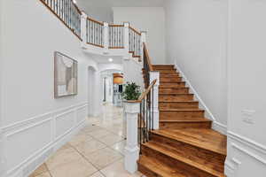 Stairs featuring a towering ceiling, crown molding, arched walkways, baseboards, and tile patterned floors