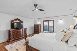 Bedroom featuring a ceiling fan, vaulted ceiling, wood finished floors, baseboards, and ornamental molding