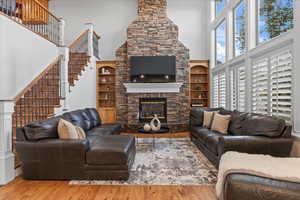 Living room featuring stairs, a fireplace, wood finished floors, and a towering ceiling