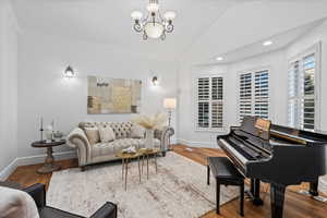 Living area featuring ornamental molding, wood finished floors, baseboards, a notable chandelier, and vaulted ceiling