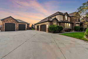 View of front of home featuring stone siding, a garage, stucco siding, a lawn, and driveway