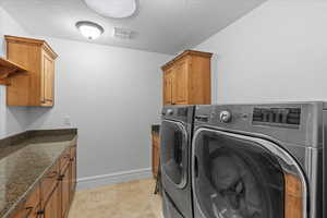 Laundry area featuring a textured ceiling, independent washer and dryer, visible vents, cabinet space, and baseboards