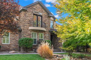 View of front of home with a front yard, a balcony, and stone siding
