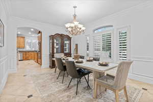 Dining area featuring ornamental molding, a decorative wall, a chandelier, arched walkways, and light tile patterned floors