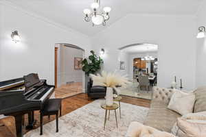 Living room with an inviting chandelier, ornamental molding, lofted ceiling, wood finished floors, and arched walkways